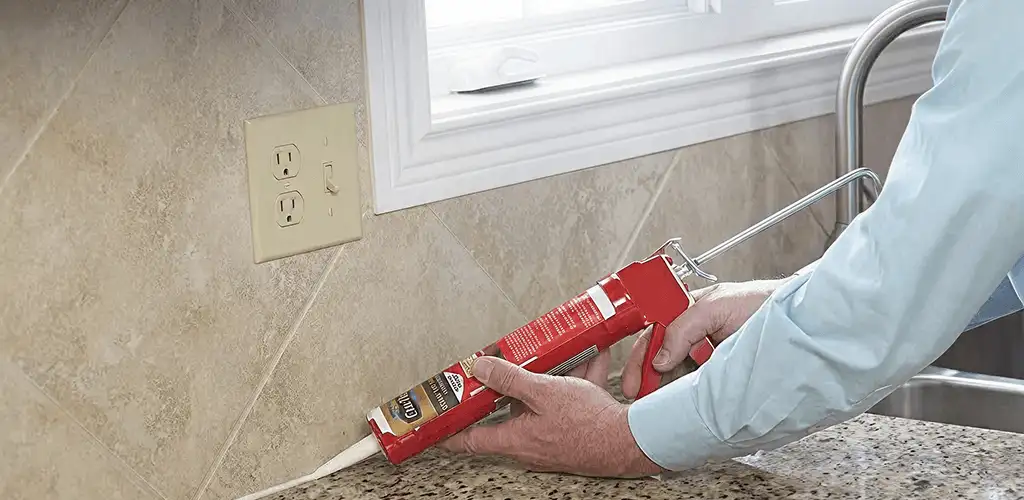 Handyman applying caulk along a kitchen backsplash and countertop seam in Saint Louis, MO