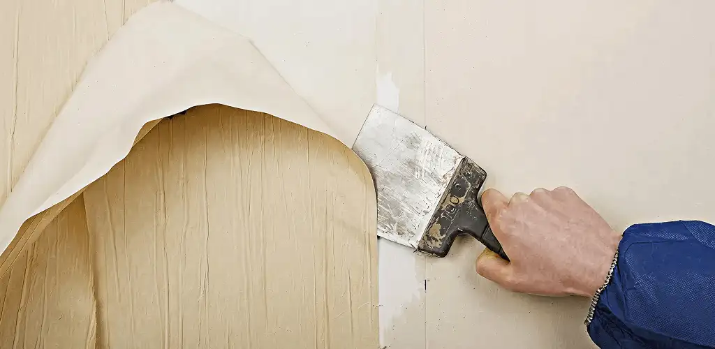 Handyman removing wallpaper with a scraper for wall preparation in Saint Louis, MO