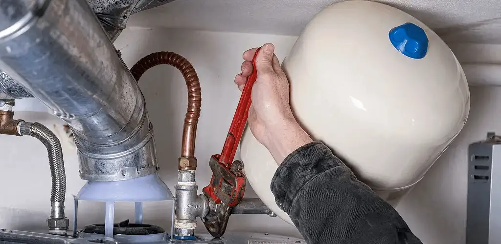 Water heater repair technician tightening plumbing connections near a tank unit in Saint Louis, MO